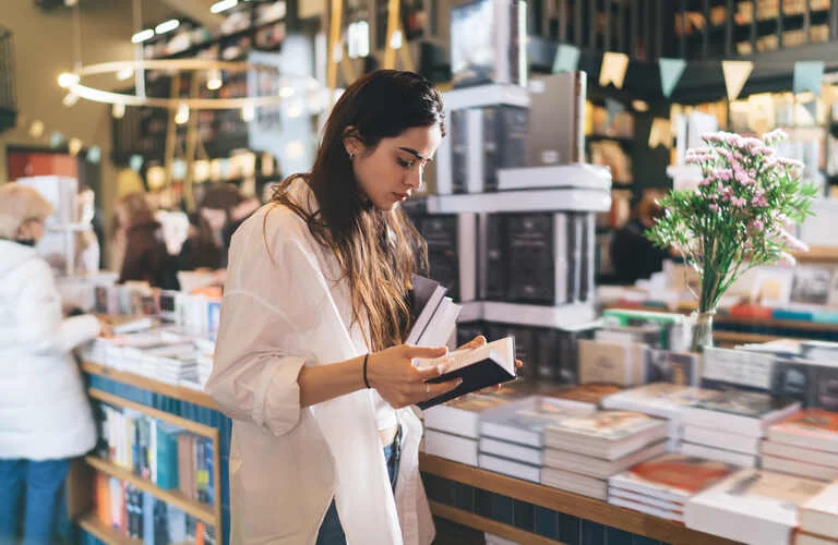 focused-woman-reading-book-while-choosing-literatu-2024-01-26-03-09-19-utc